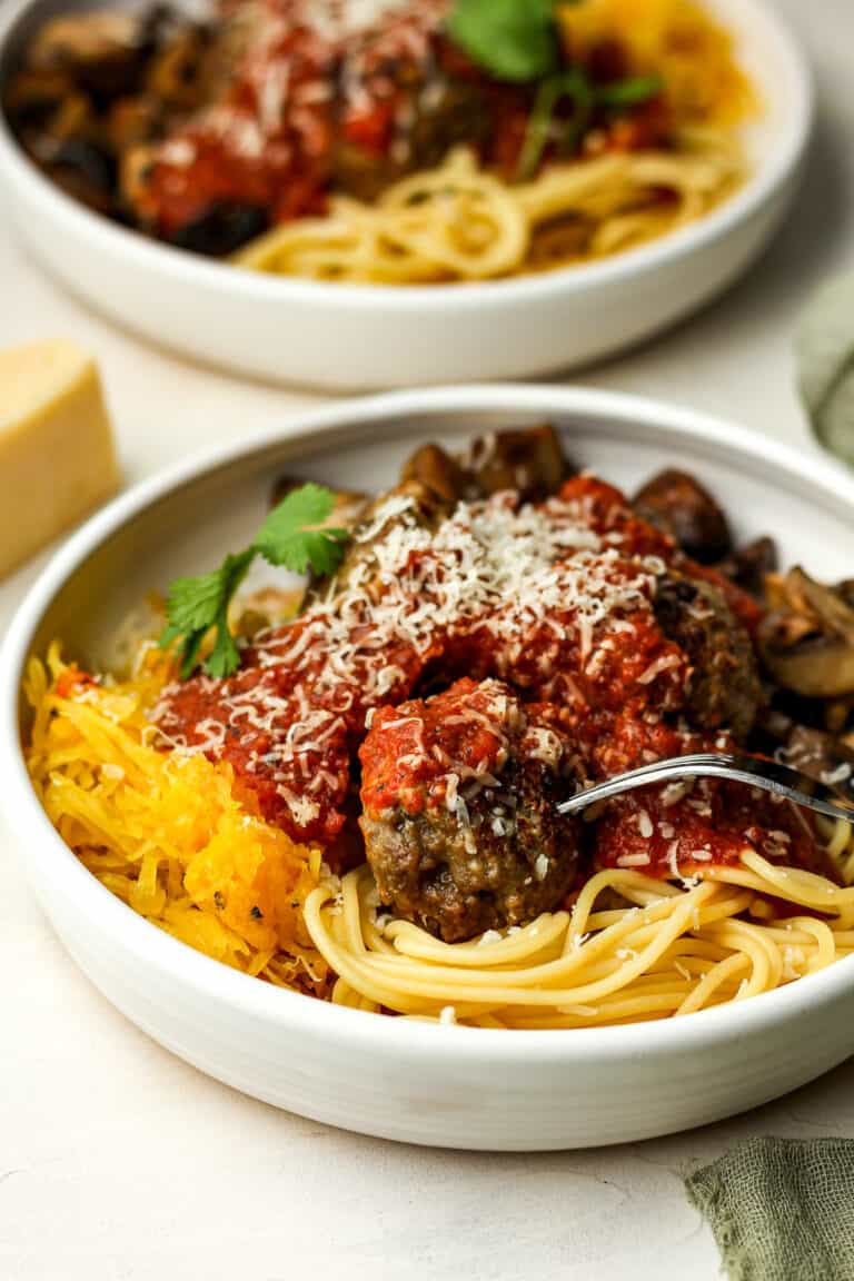 Side view of two bowls of spaghetti and meatballs plus marinara and veggies.