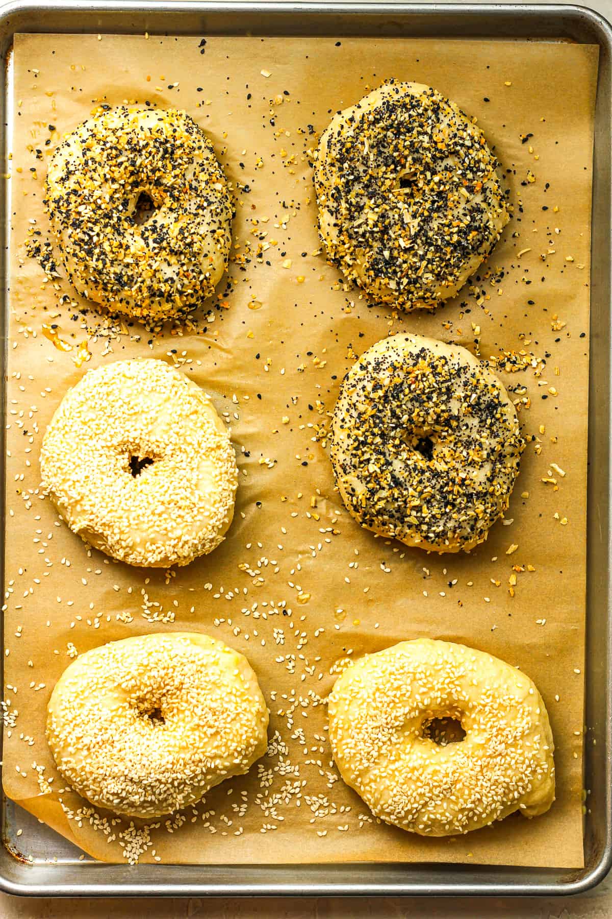 A baking sheet with six bagels with toppings before baking.