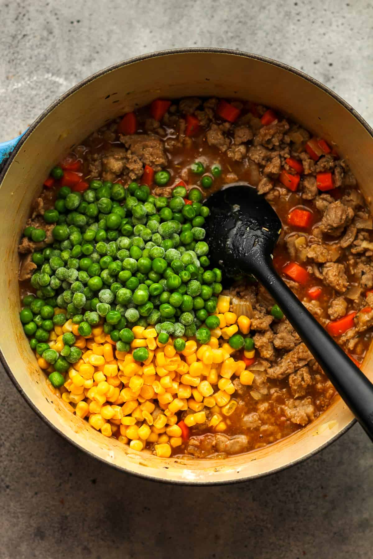 A pot of the browned turkey with frozen peas and corn on top.