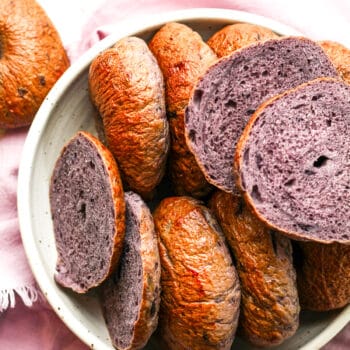A bowl of blueberry bagels with some sliced open showing the purple insides.