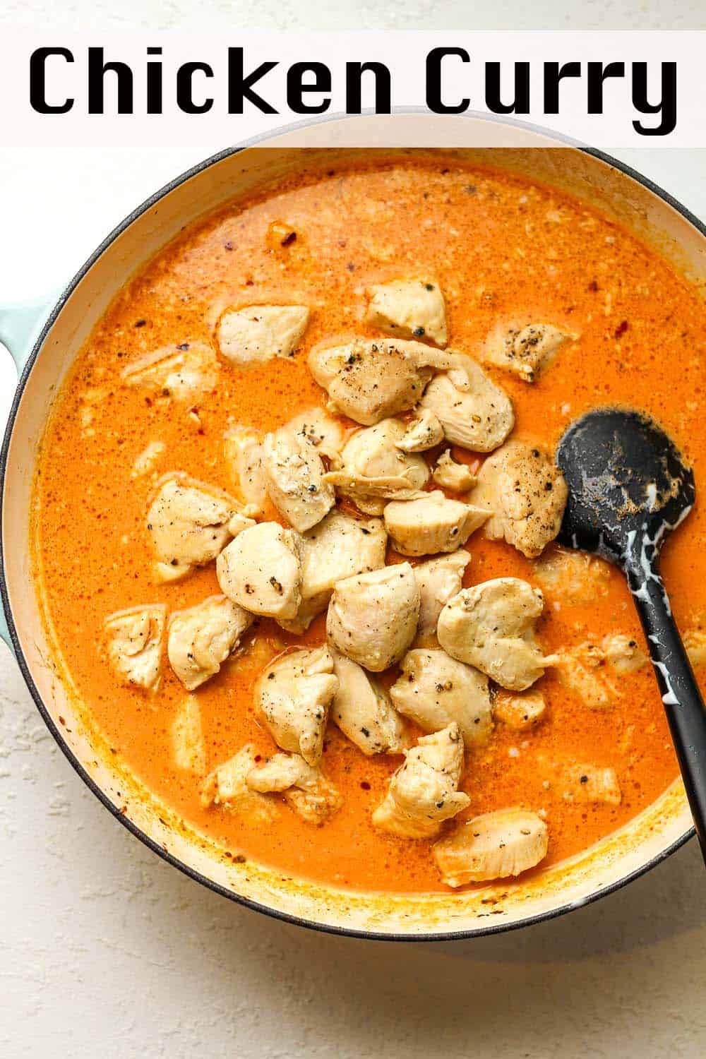 A braiser with red curry sauce and chicken pieces on top.