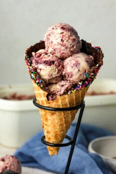 A waffle cone filled with black cherry ice cream in an ice cream stand.
