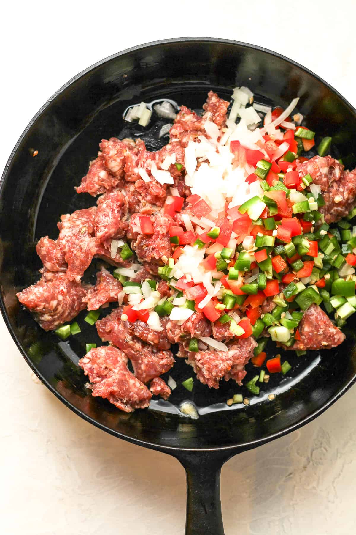 A skillet of the raw sausage, onions, and peppers.