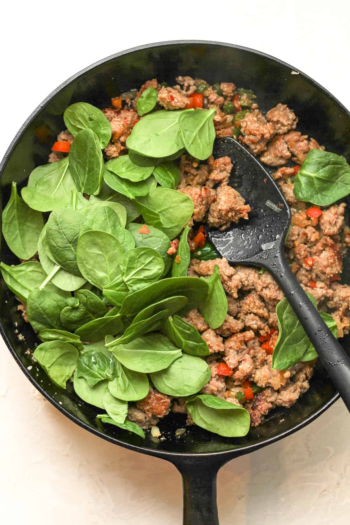 A skillet of the cooked sausage with spinach added on top.
