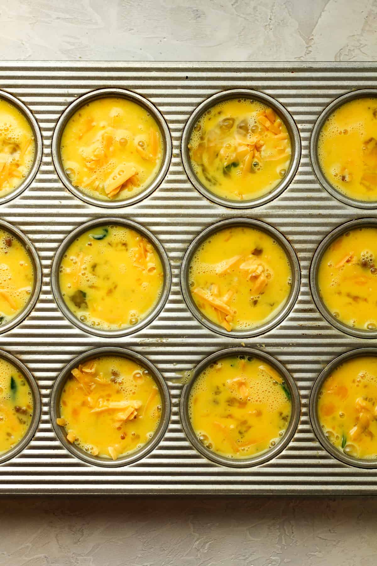 A muffin tin with the ingredients in cups before baking.