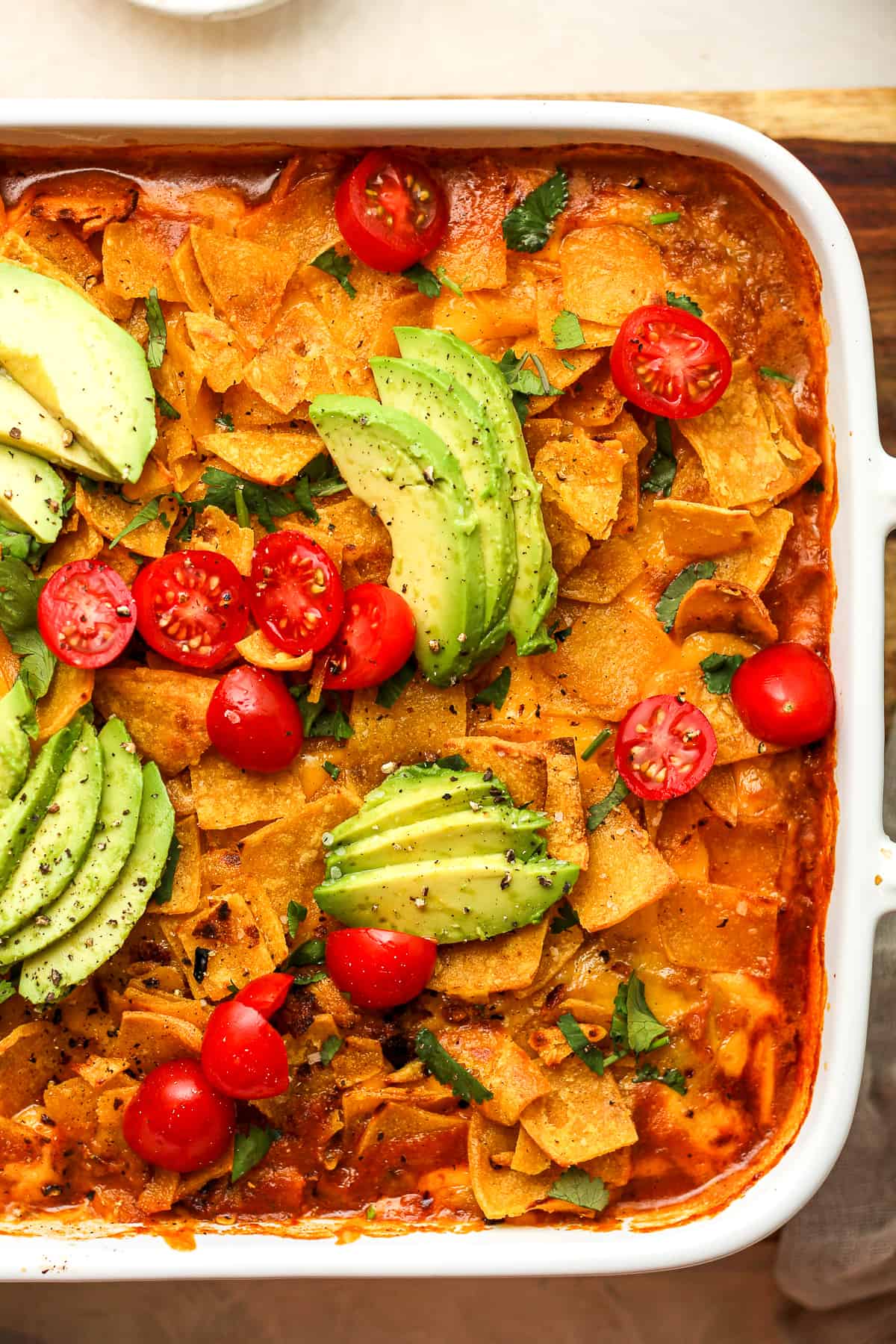 Closeup on a square casserole of walking taco casserole with avocado and tomato on top.