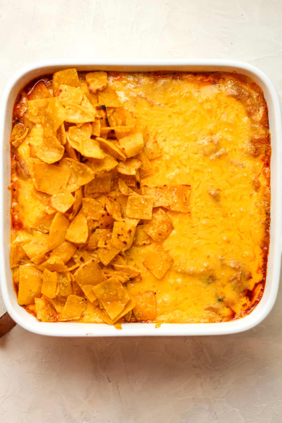 A dish of the casserole with melted cheese on top and some of the sautéed corn tortillas.