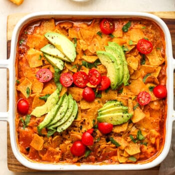 A square dish of walking taco casserole with sliced avocado on top.