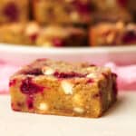 Side view of a chewy blondie with white chocolate chips and raspberries.