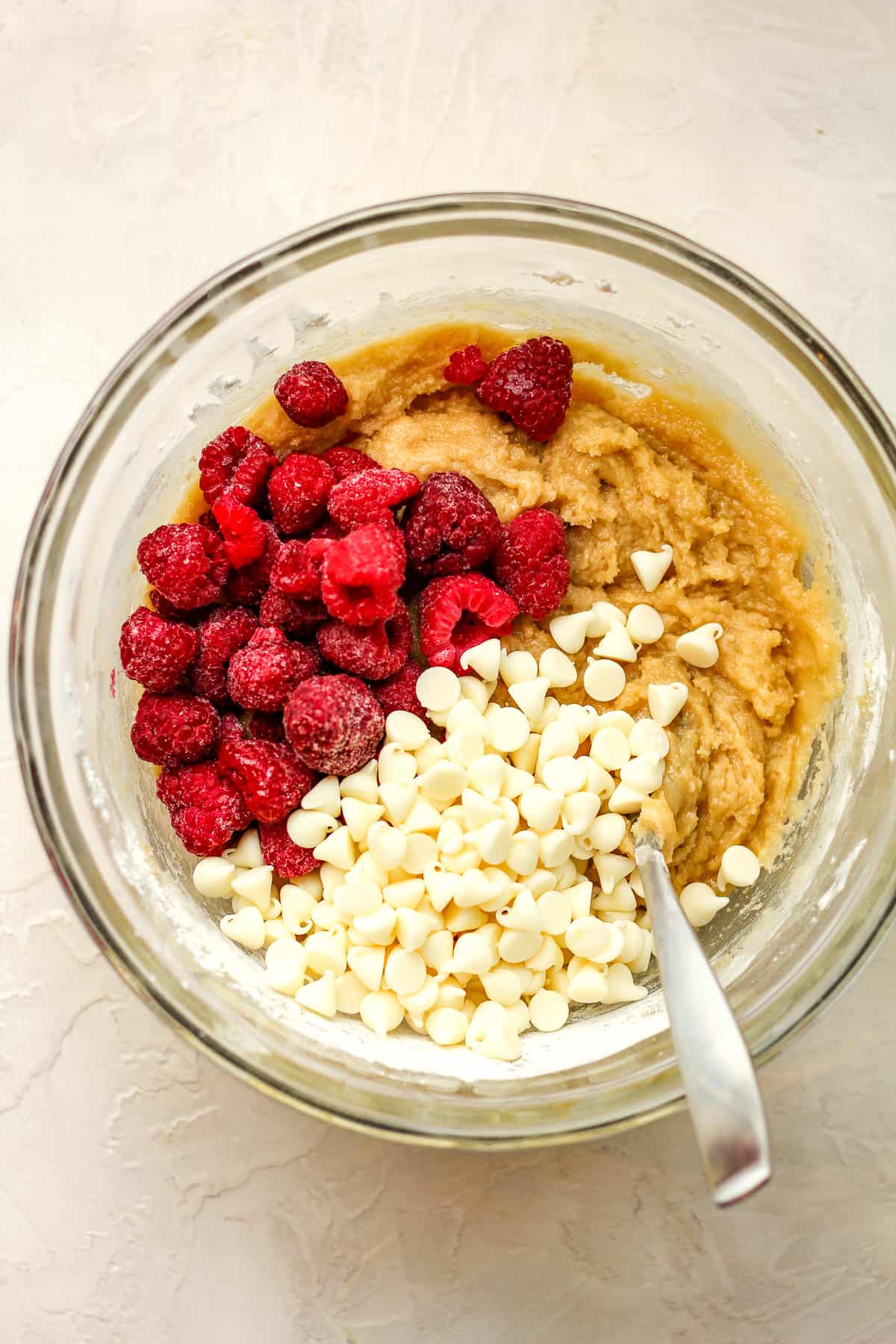 A bowl of the batter plus white chocolate chips and frozen raspberries.