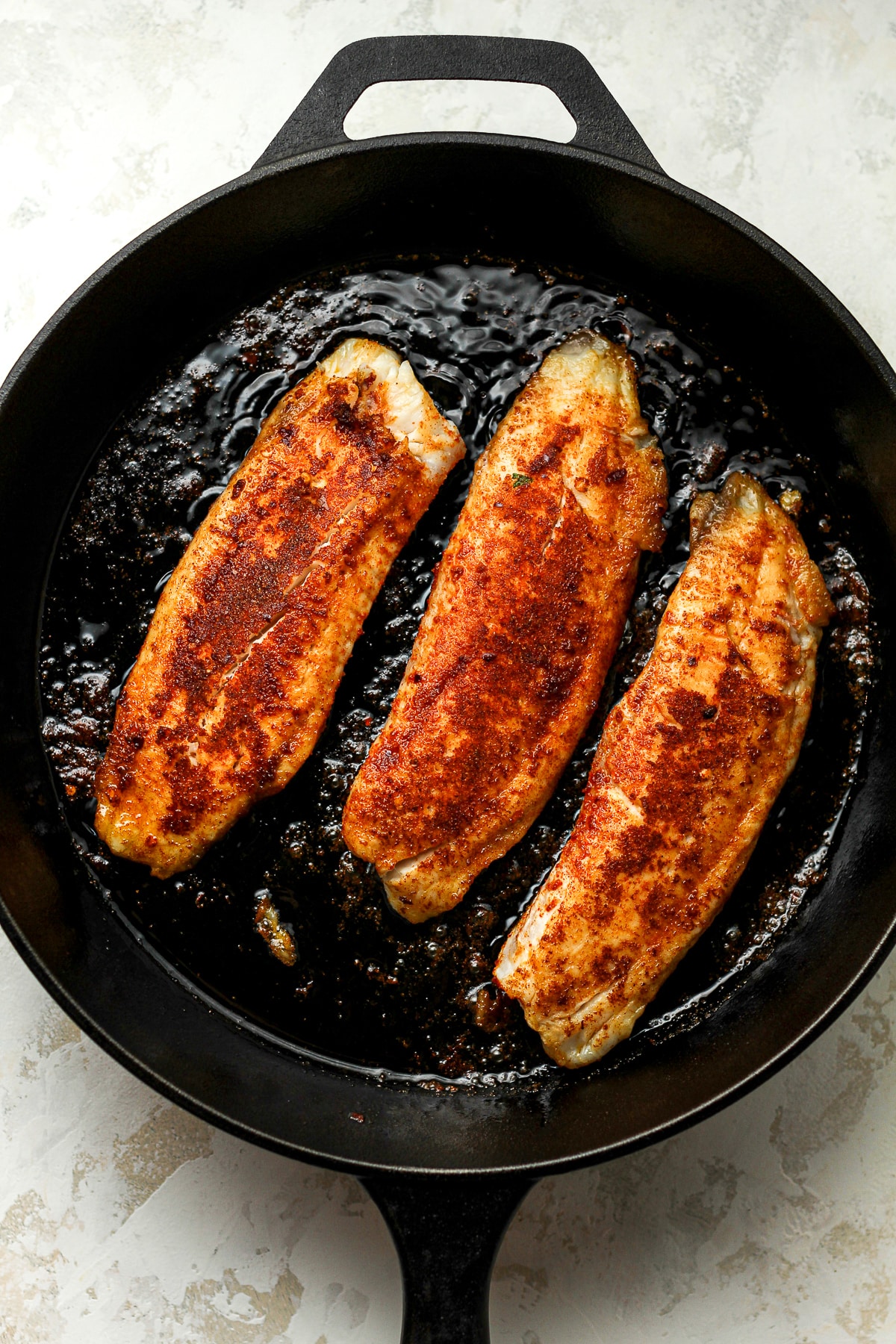 A cast iron skillet with three filets of blackened tilapia.