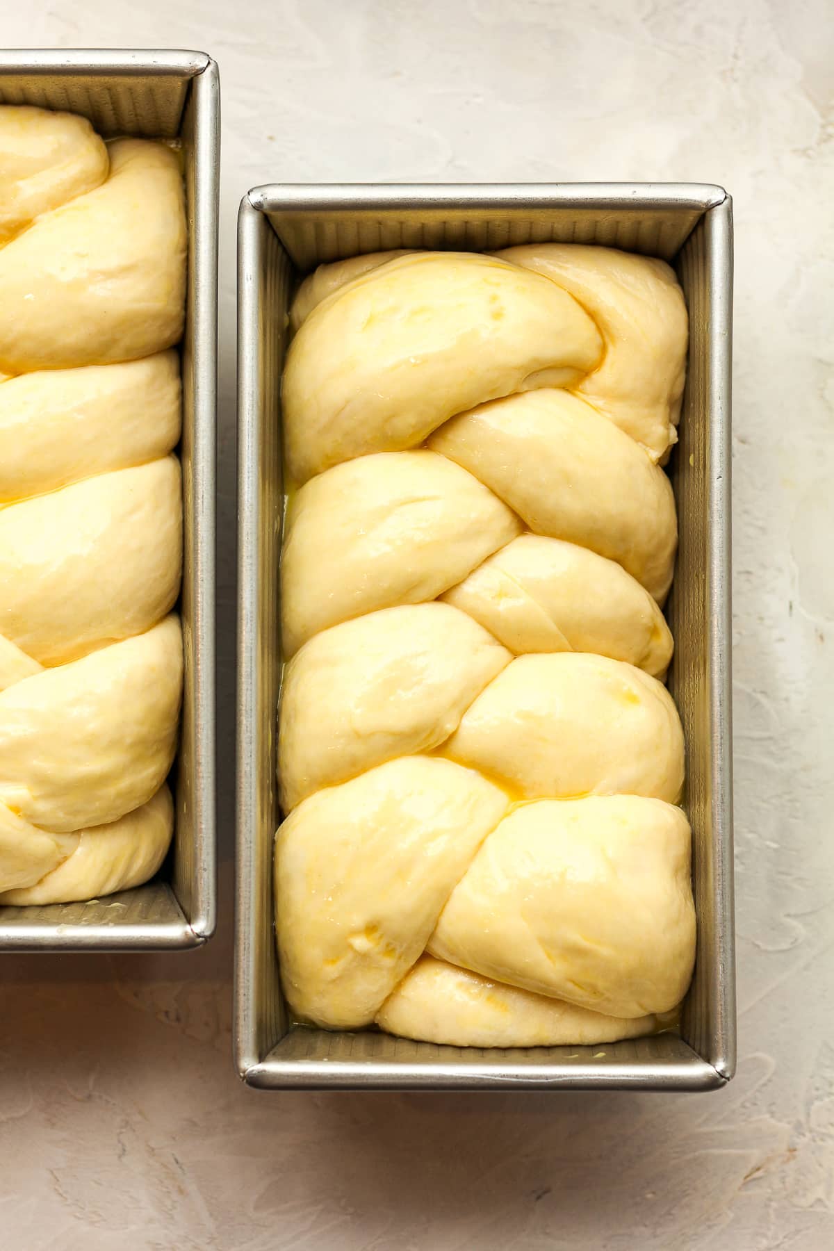 Two loaf pans of braided brioche bread.