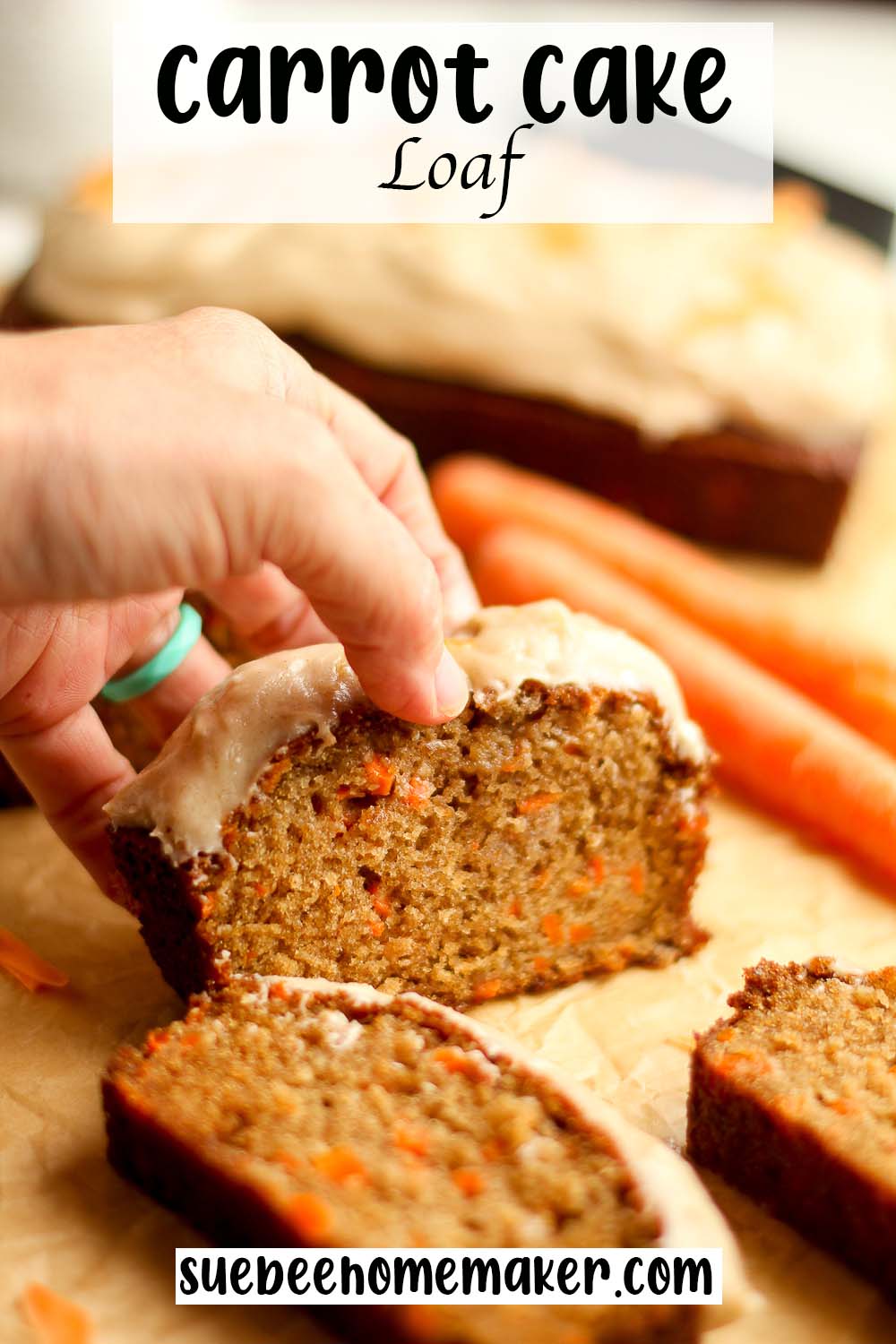 Side view of a hand lifting up a slice of iced carrot cake loaf.