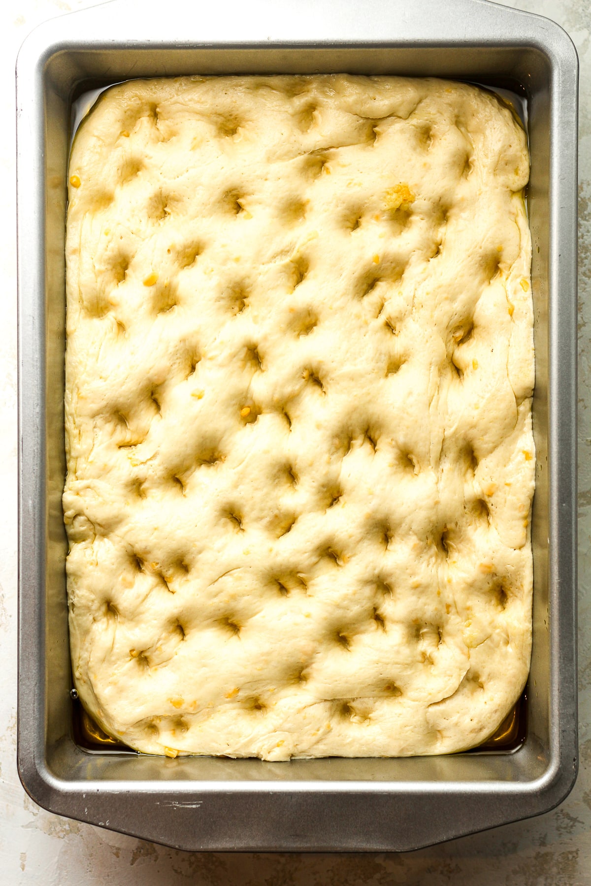 A pan of the focaccia dough with dimples.