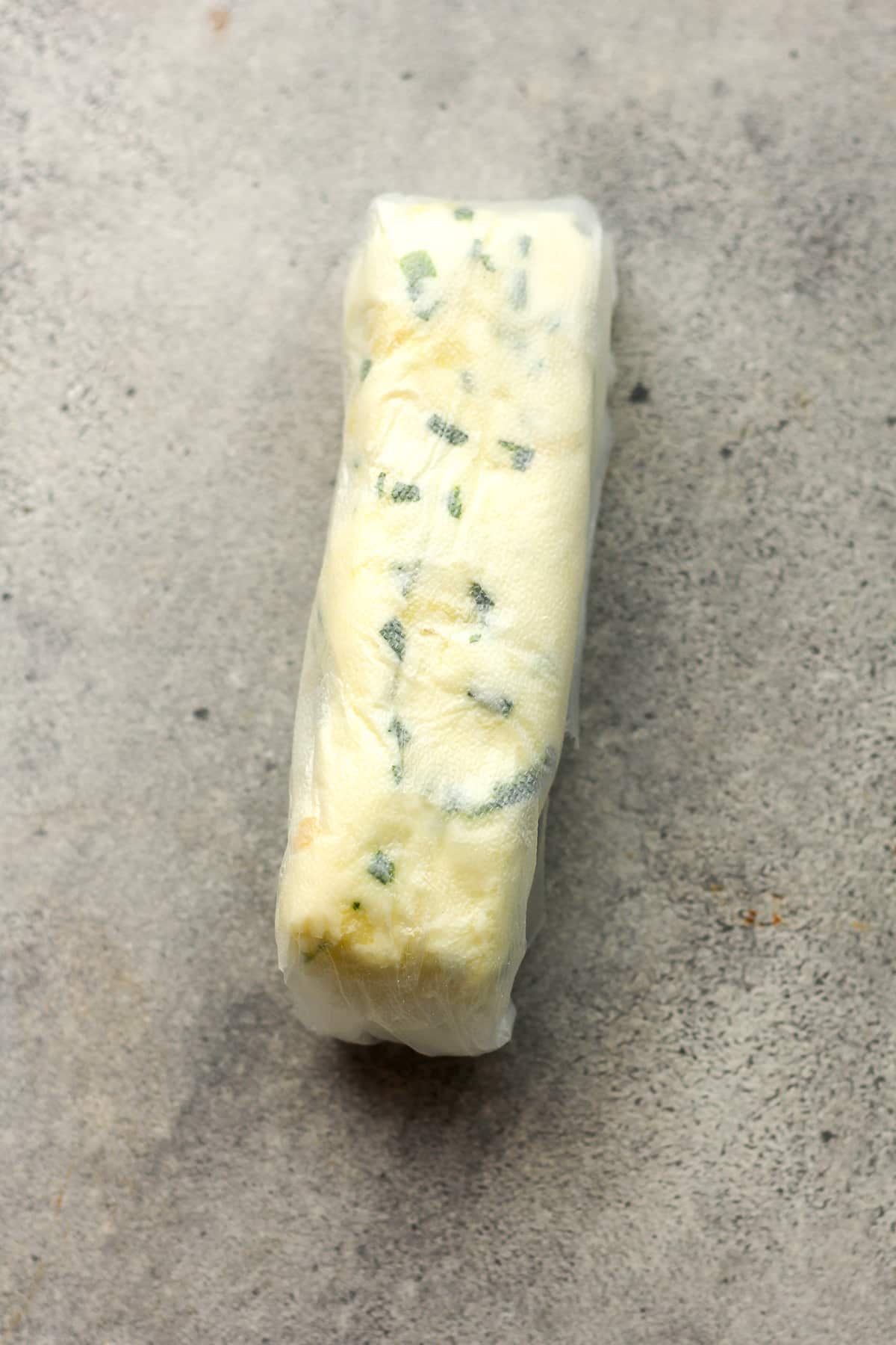 A log of garlic butter with chives wrapped in cling wrap.