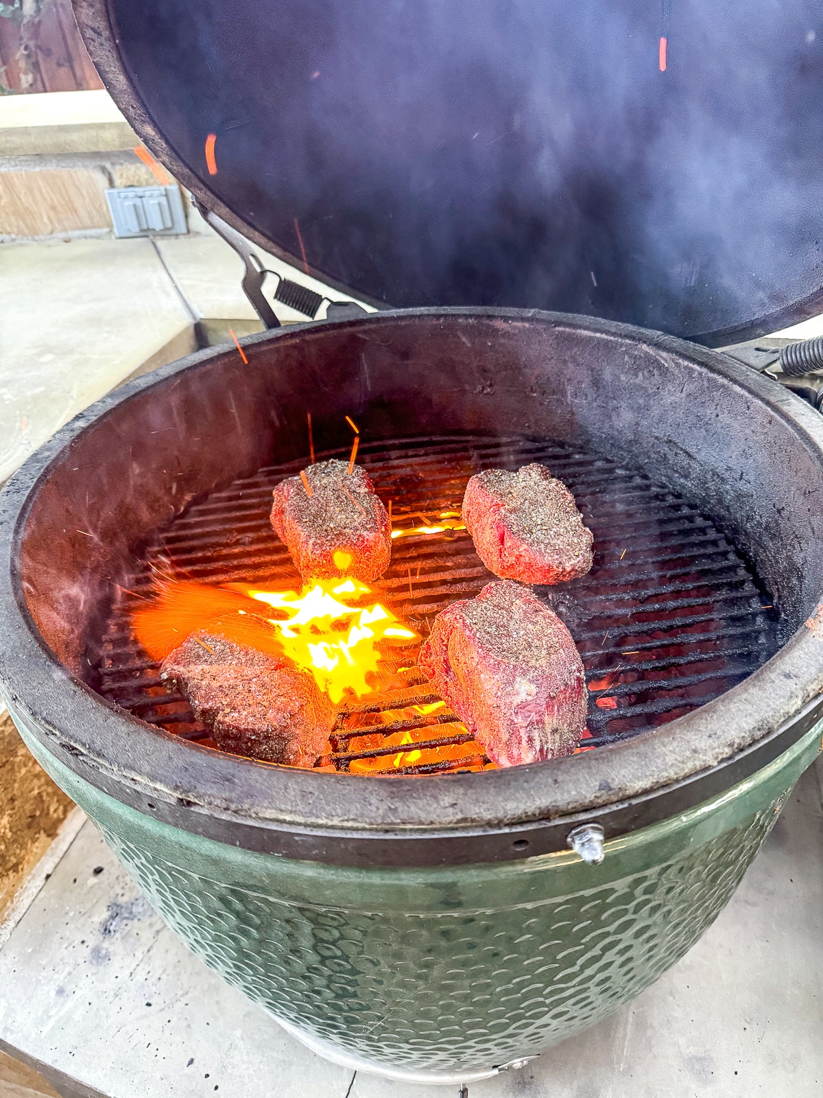 Overhead view of a Big Green Egg with four filets on it over a very hot fire.