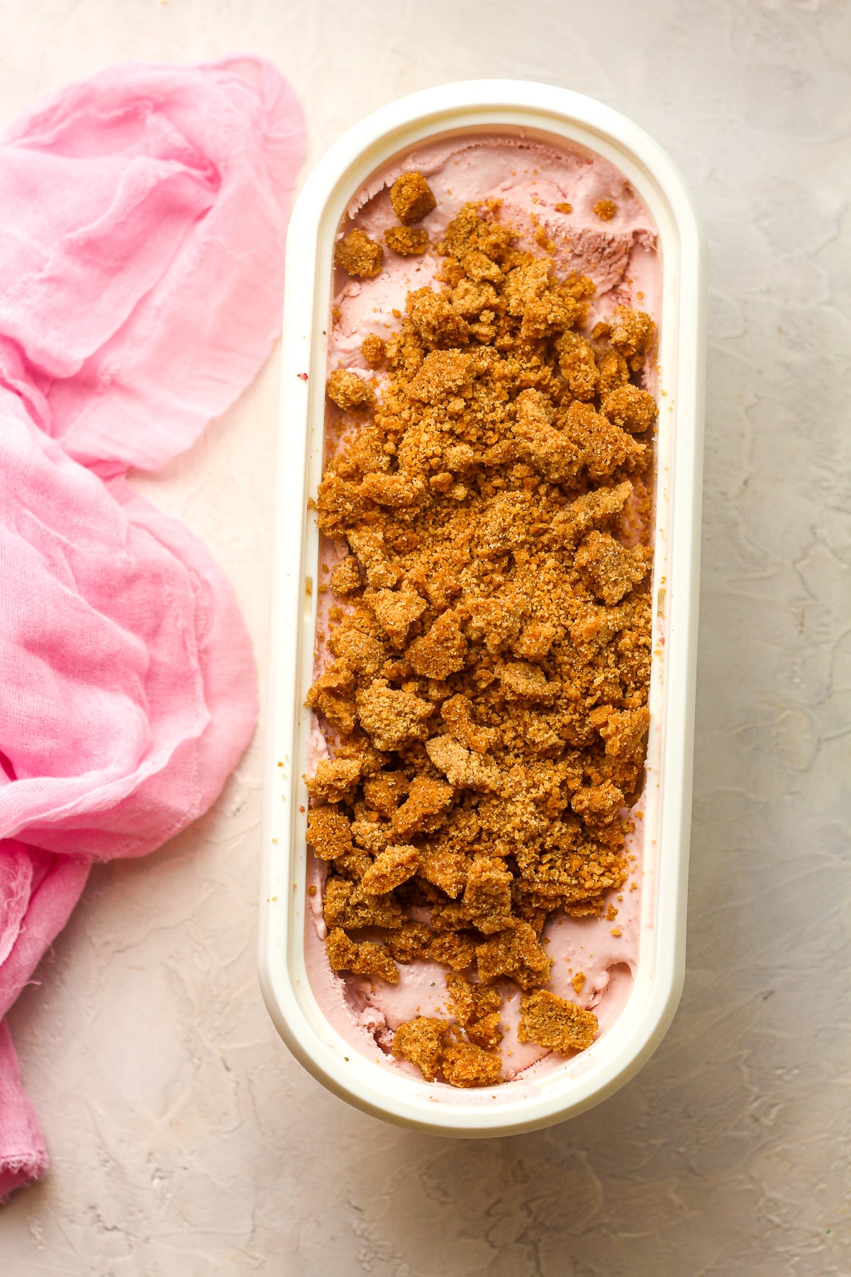 An oblong container of strawberry ice cream with graham cracker crumbles on top.
