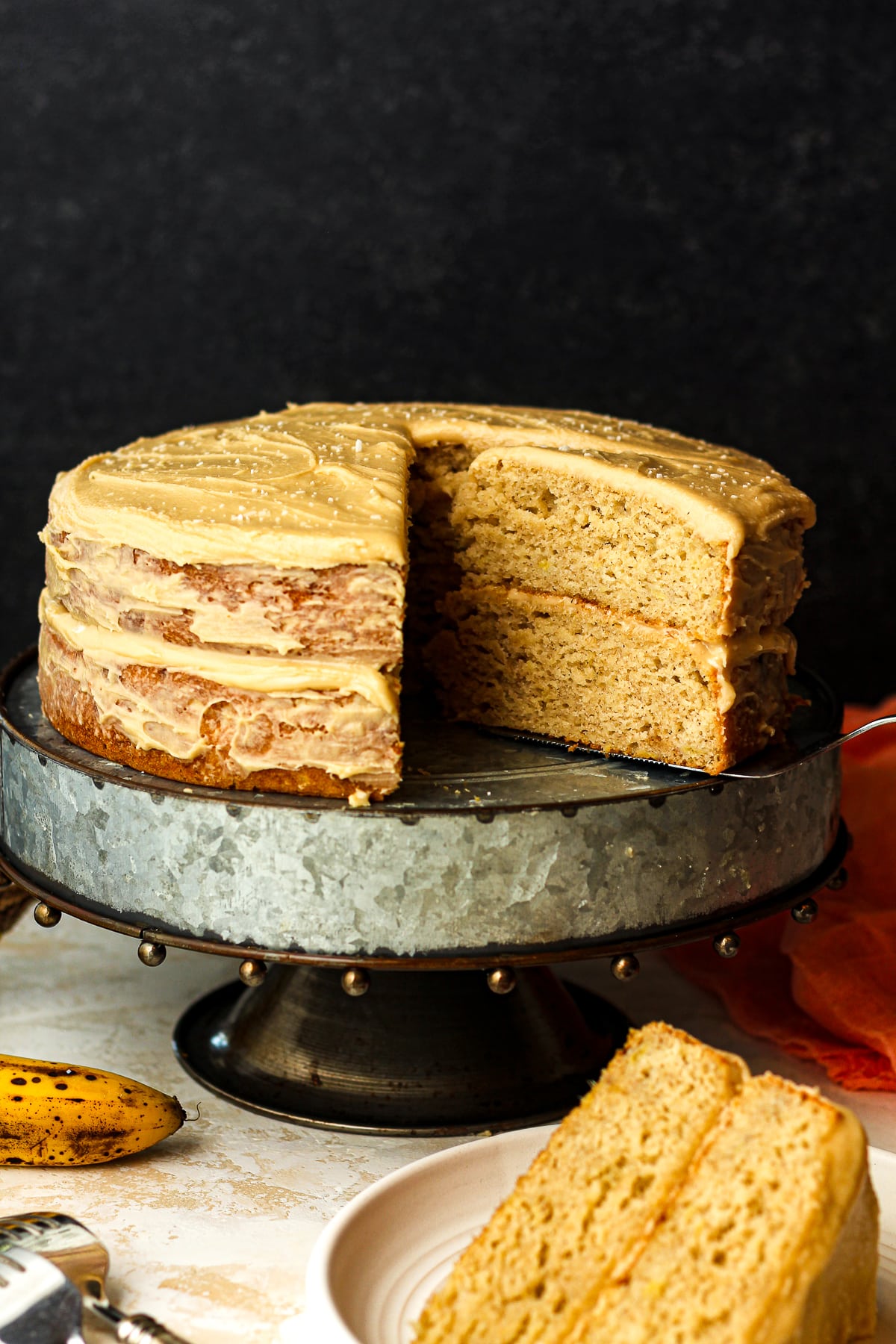 Side view of a naked layered banana cake on a silver cake stand.
