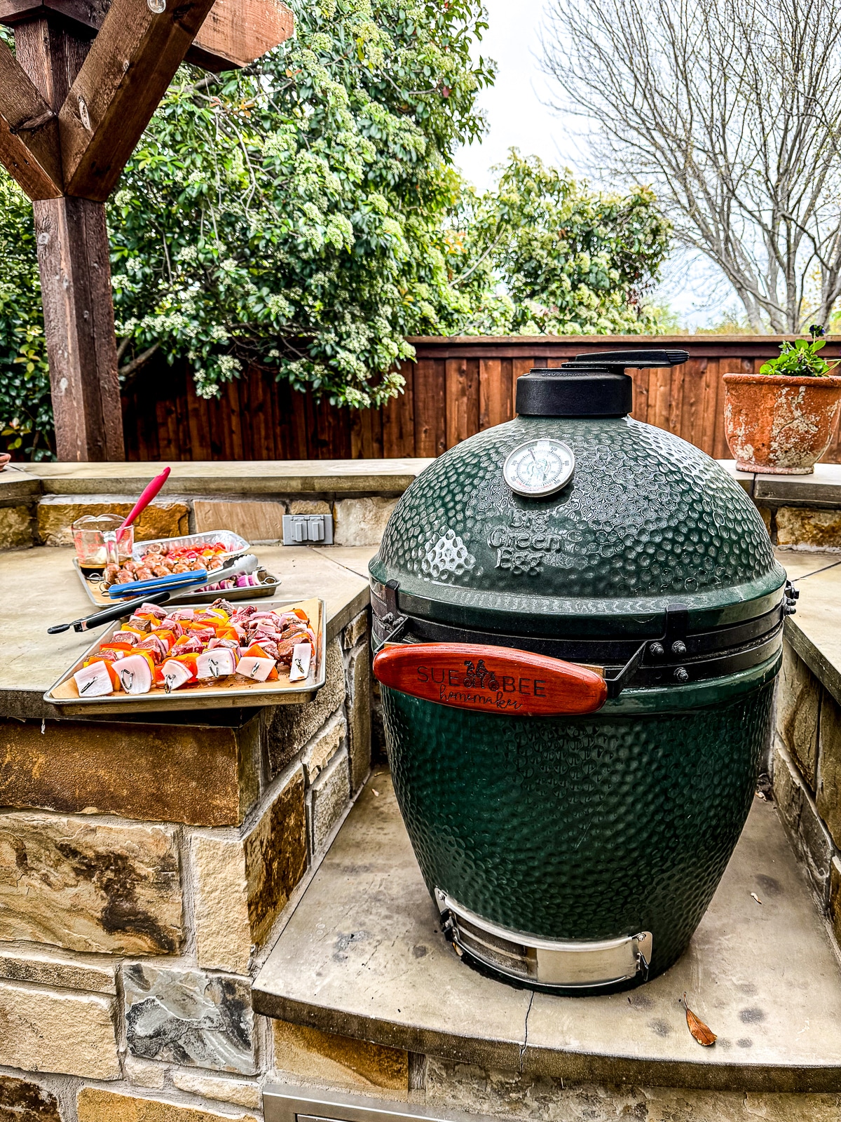 A Big Green Egg with the trays of food next to it.