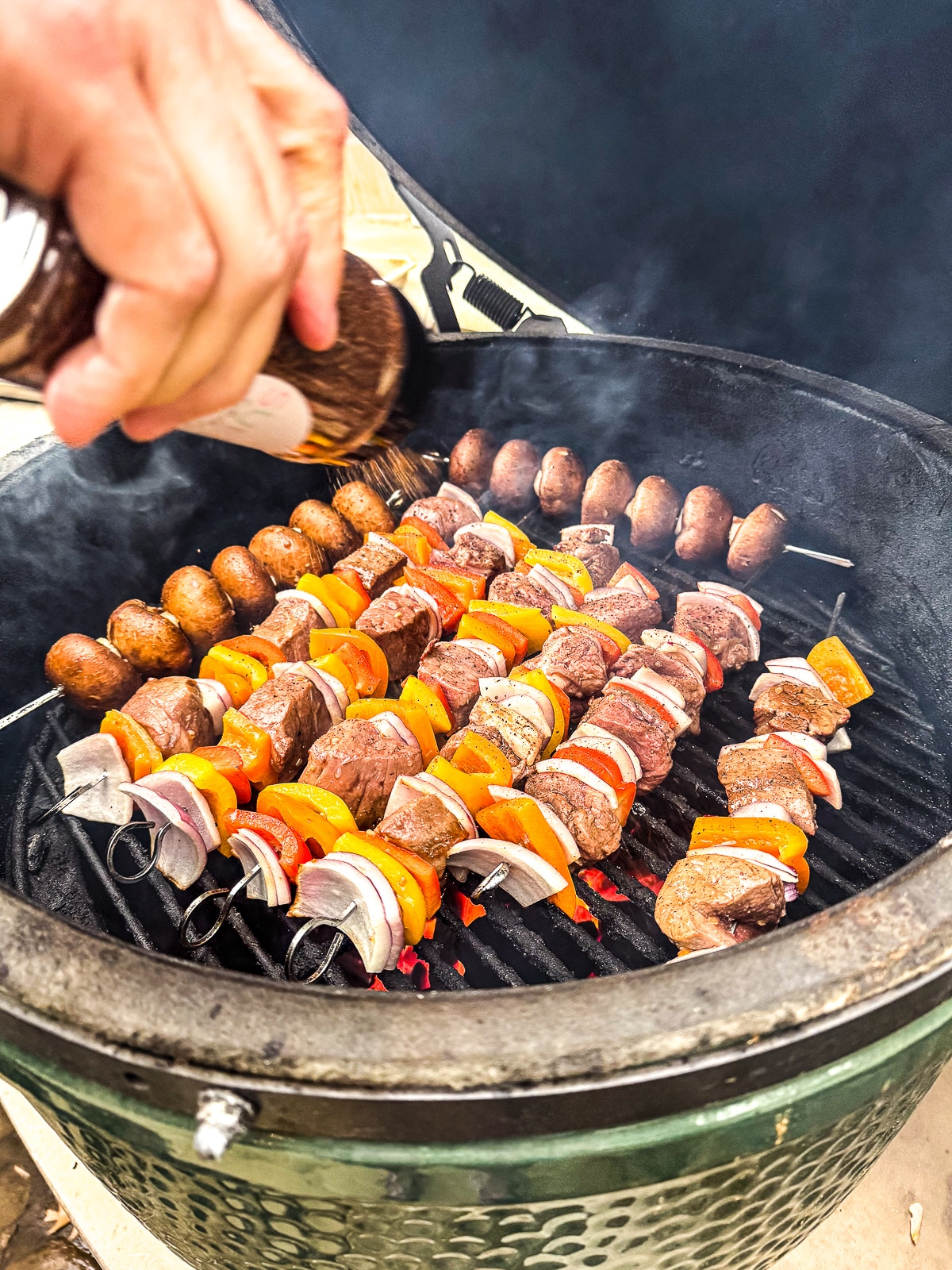 A grill with the beef kabobs and some seasoning being added.