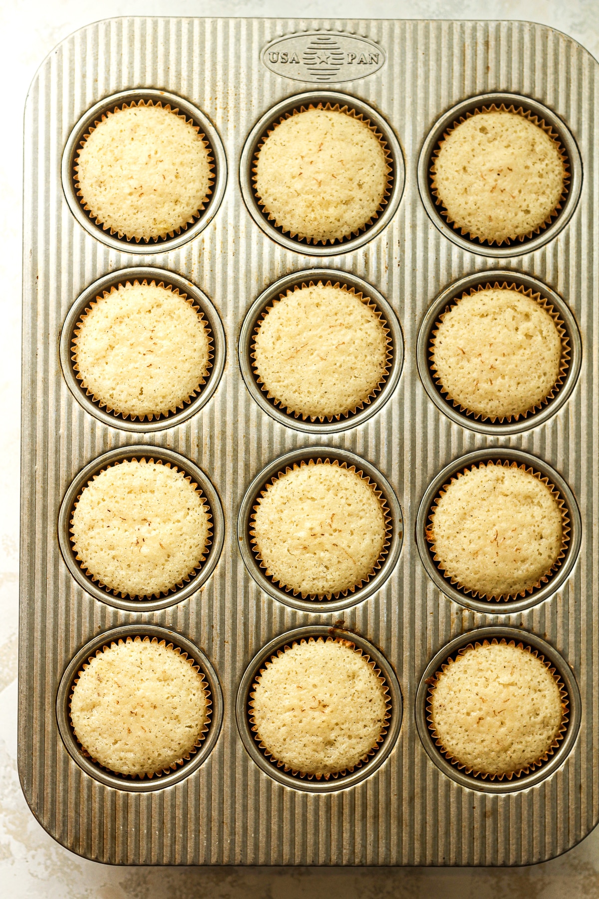 A muffin tin with baked vanilla cupcakes.