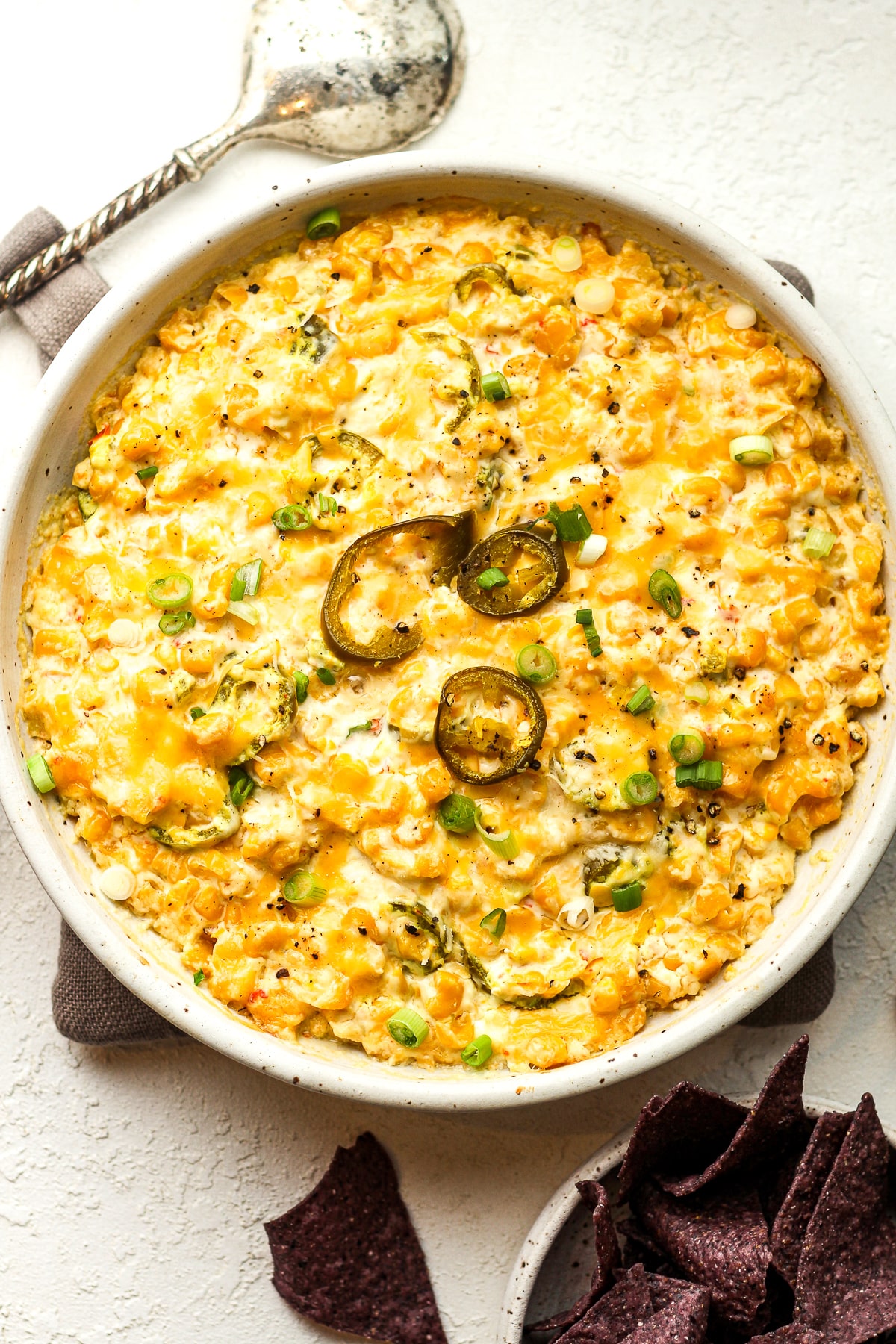 A bowl of corn dip with sour cream and jalapeños.