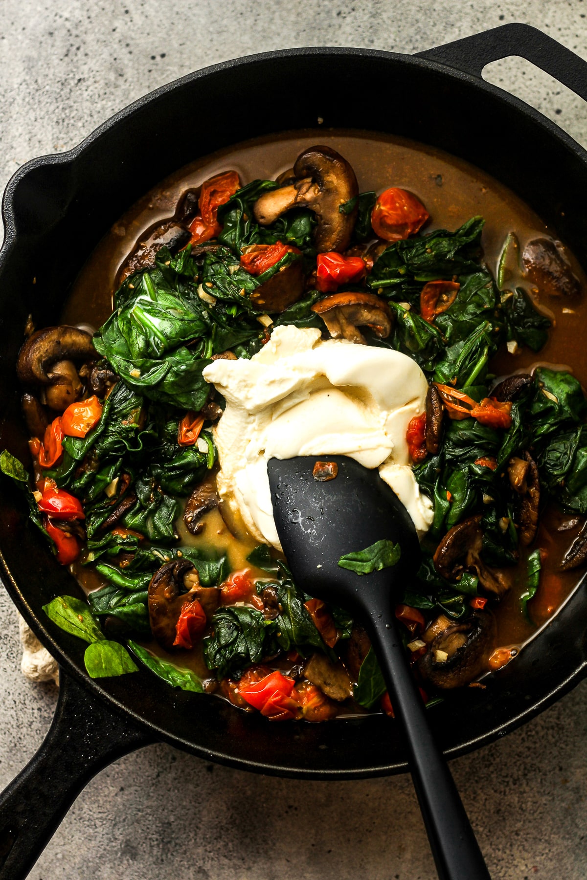 A skillet of the veggies with ricotta. cheese on top.