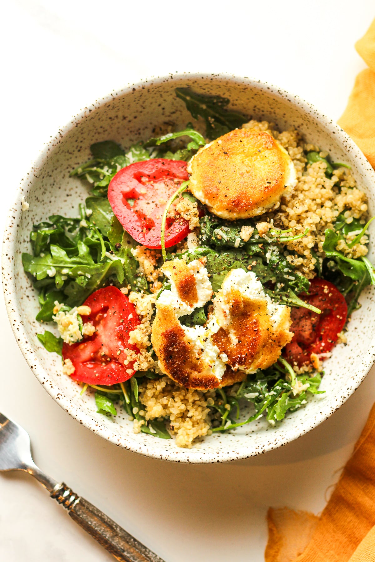 A bowl of arugula and quinoa salad with fried goat cheese.