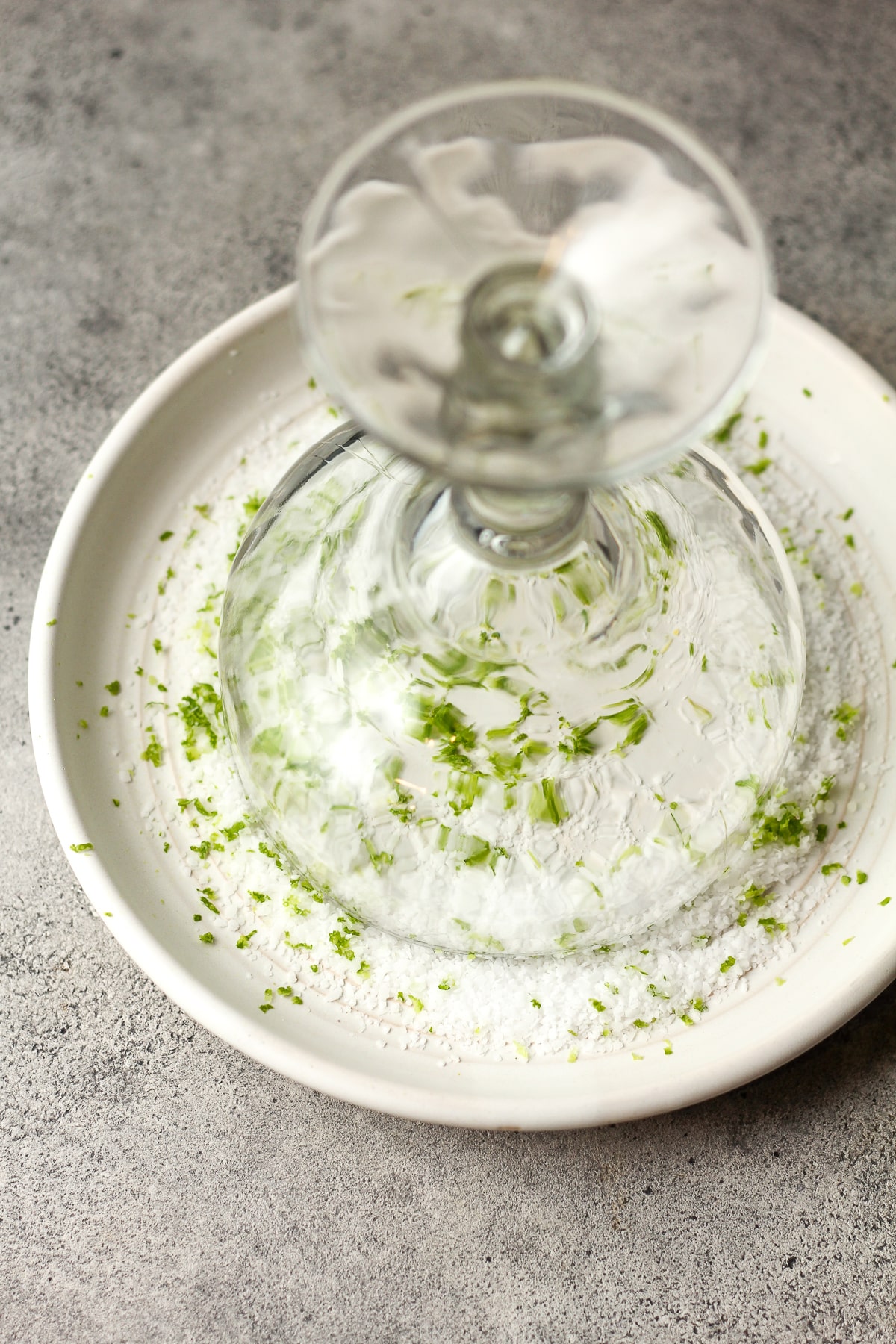 A margarita glass turned upside down on a plate of salt and lime zest.