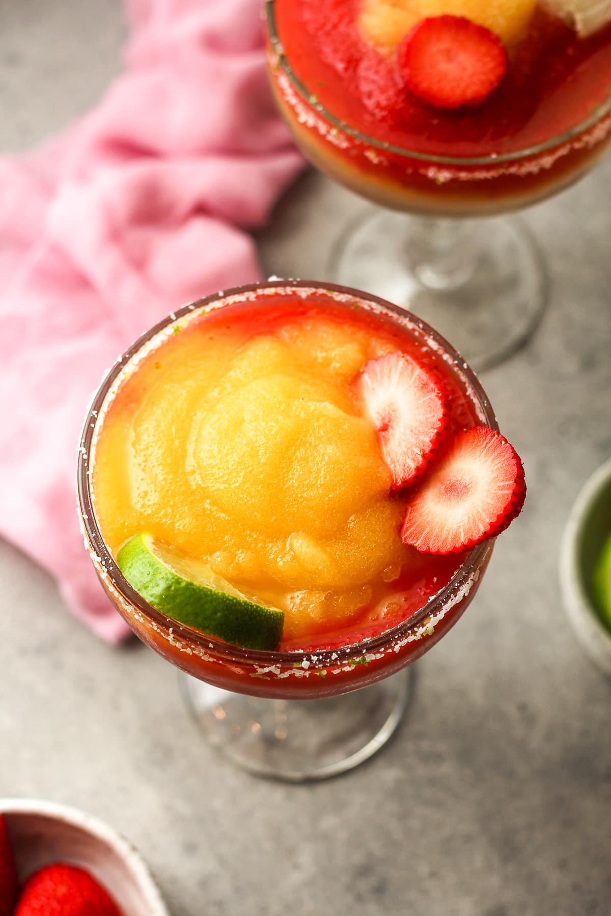 Overhead view of two frozen margaritas with blended strawberries and peaches.