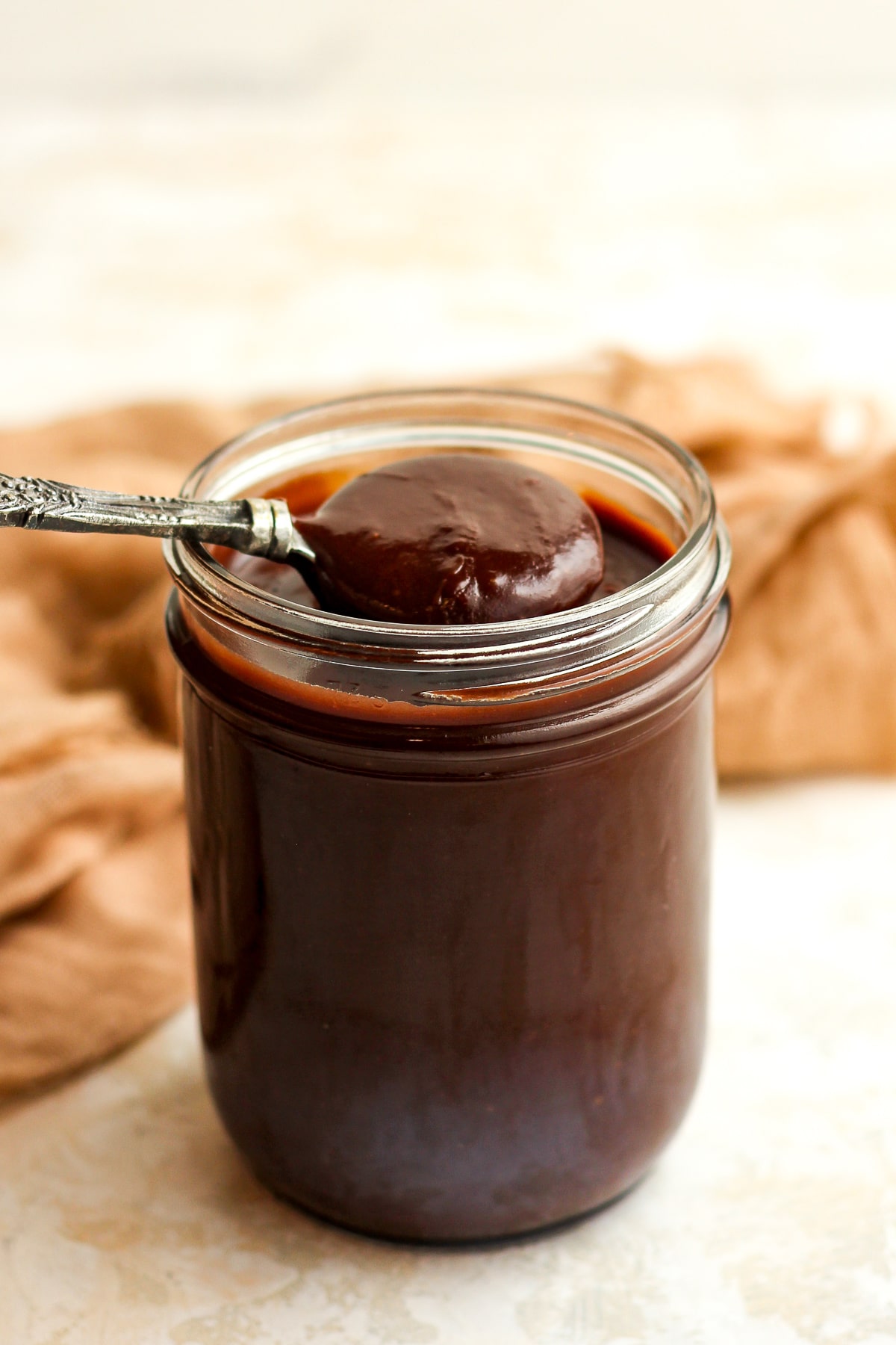 Side view of a jar of hot fudge sauce with a spoonful on top.
