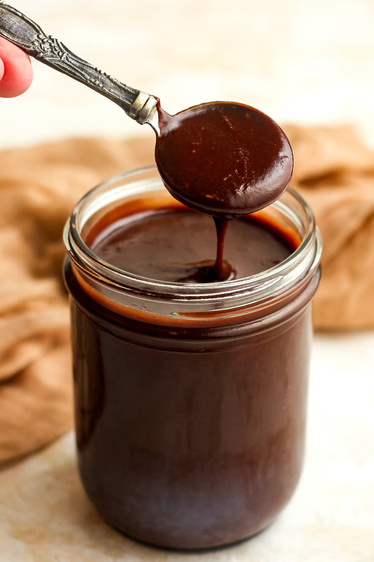 A spoonful of hot fudge sauce above a full jar.