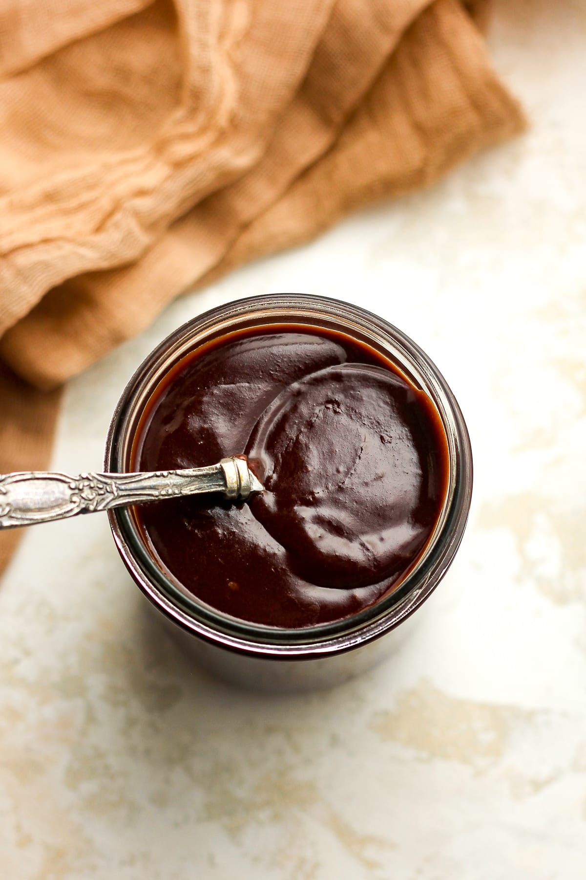 Overhead view of a jar of hot fudge sauce with a tablespoon on top.