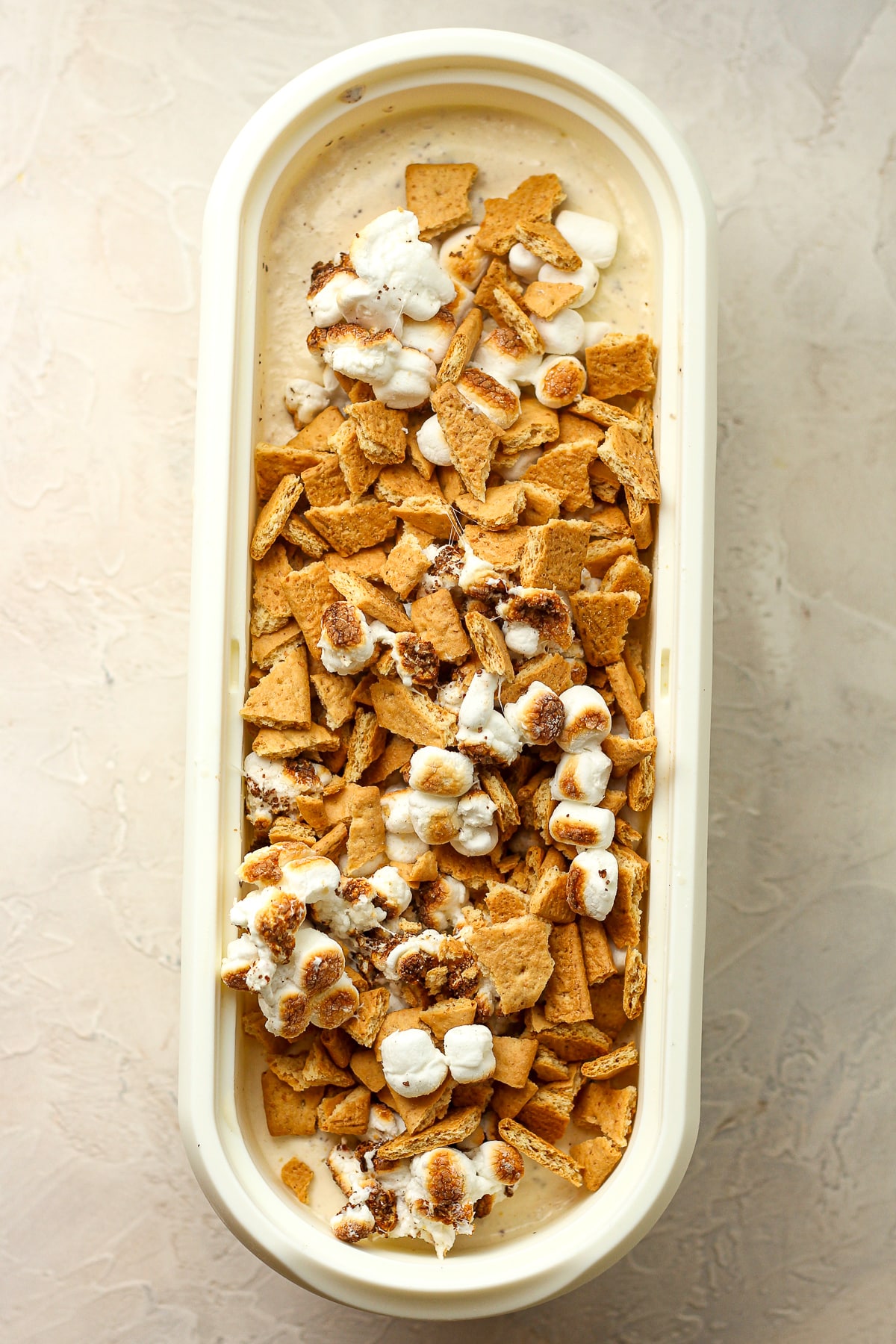 An oval container of the ice cream base with toasted marshmallows and graham cracker pieces on top.