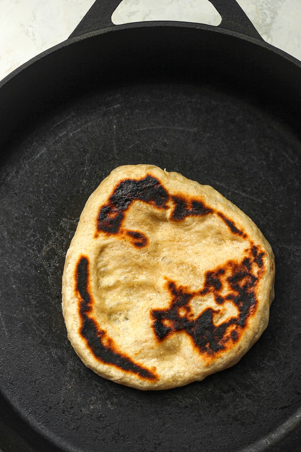 A sourdough naan cooking on a cast iron skillet.