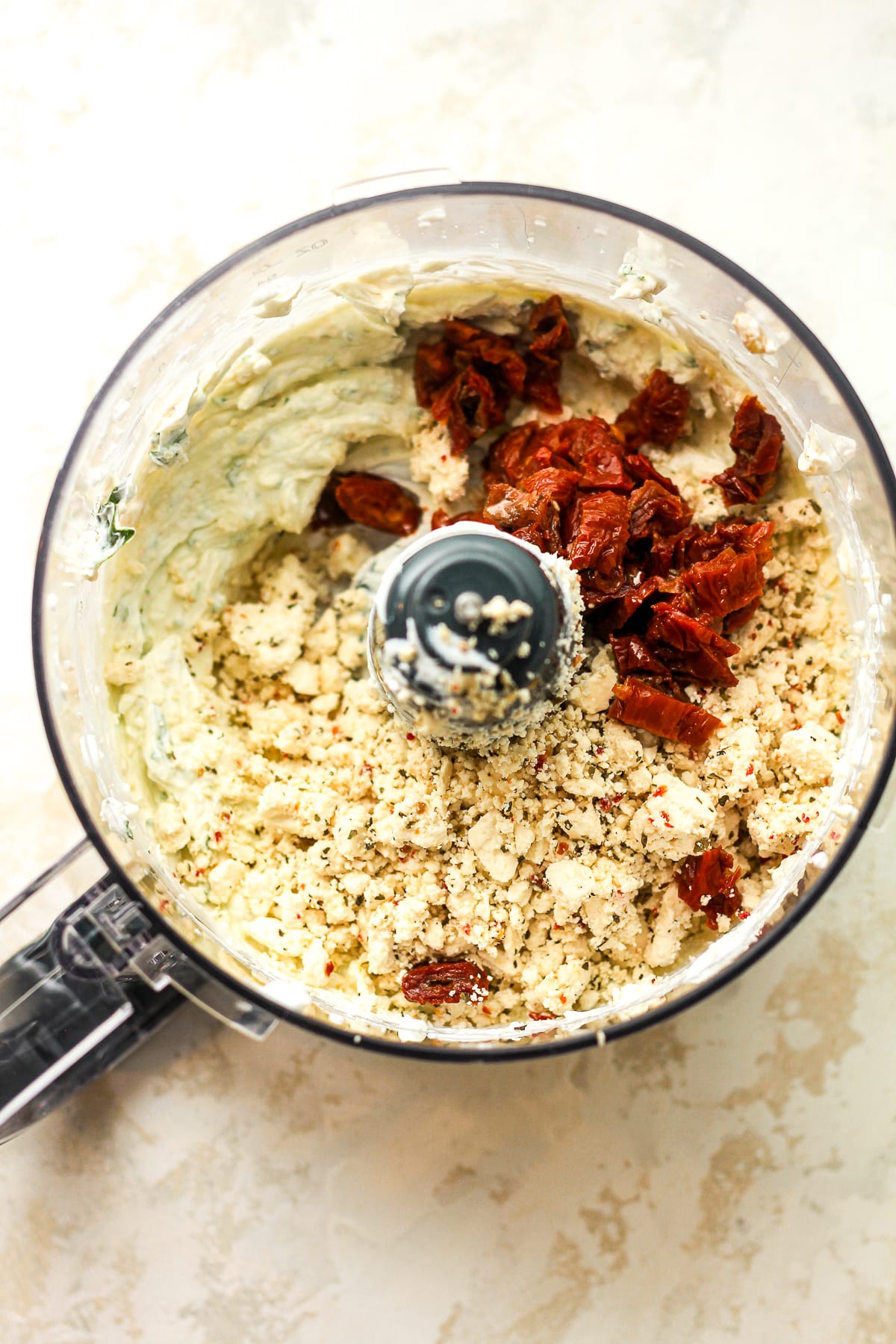 A food processor of the creamy ingredients plus feta crumbles and sun dried tomatoes on top.