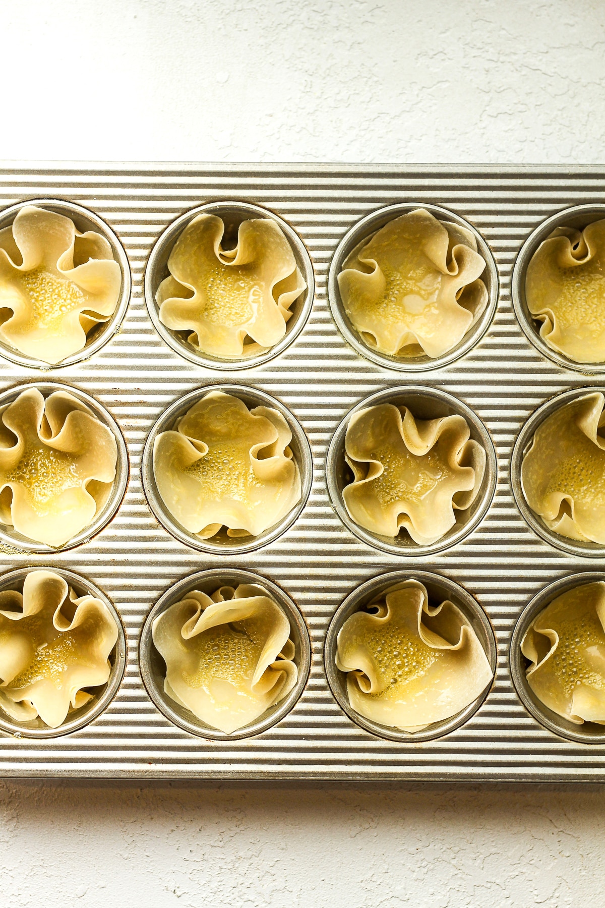 A muffin pan with two wonton wrappers in each cup and sprayed with baking spray.
