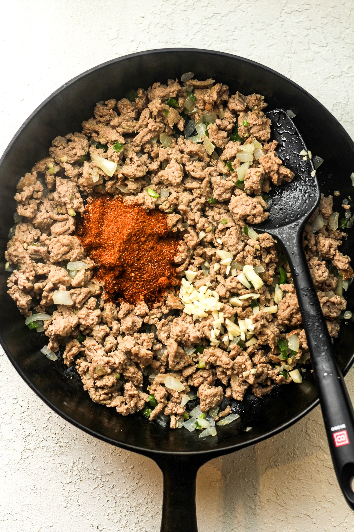 A skillet of the browned meat with the garlic and taco seasoning on top.