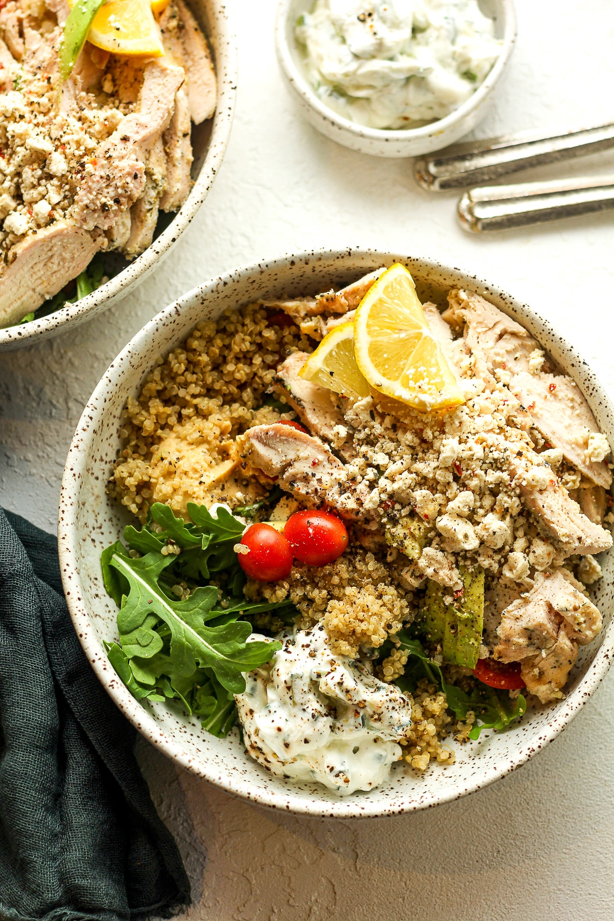Two bowls of quinoa, Greek chicken, hummus, and tzatziki sauce.