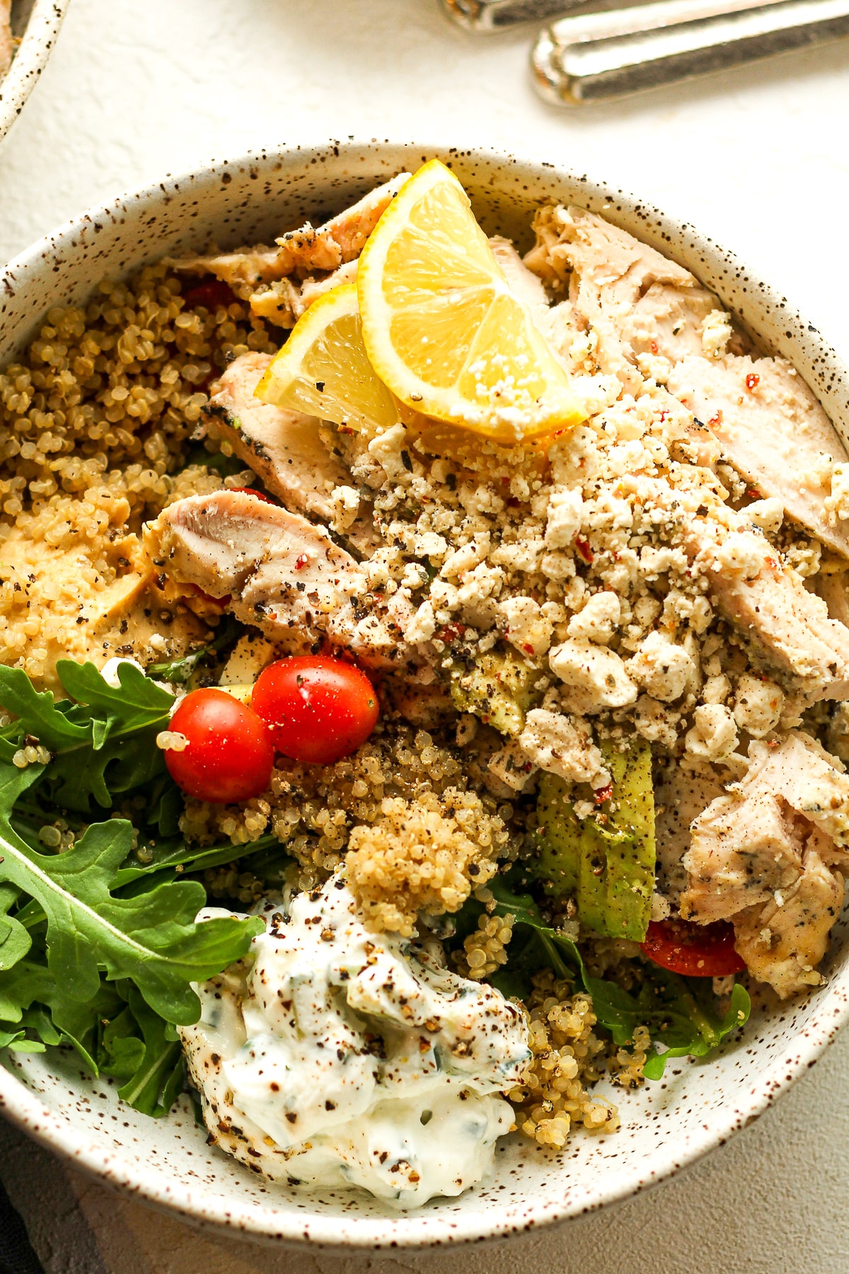 Closeup on a Greek chicken bowl with quinoa, tzatziki sauce, hummus, and feta.