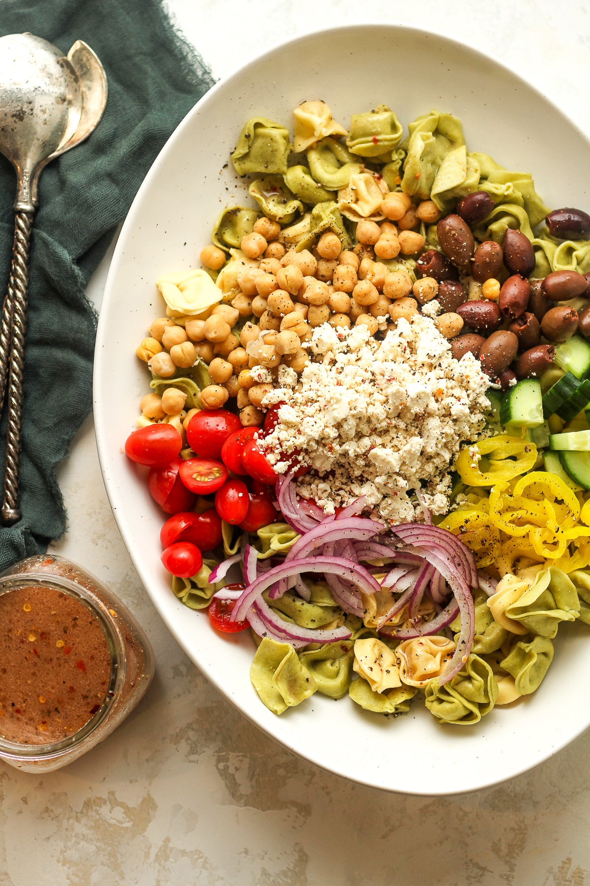 An oblong bowl of the pasta salad ingredients separated by ingredient with a jar of dressing.
