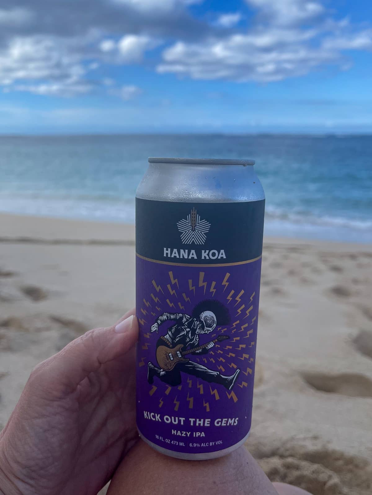 My hand holding an IPA by the beach.