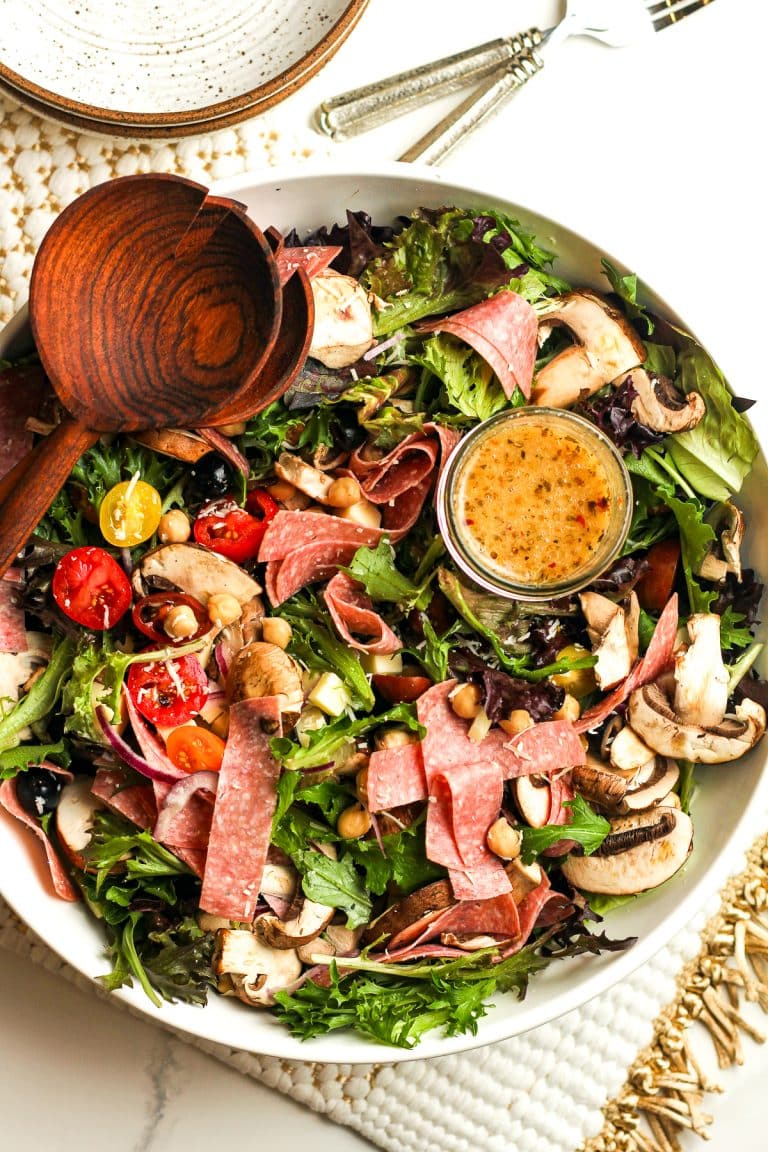 A bowl of the antipasto salad with a jar of dressing and some wooden spoon.