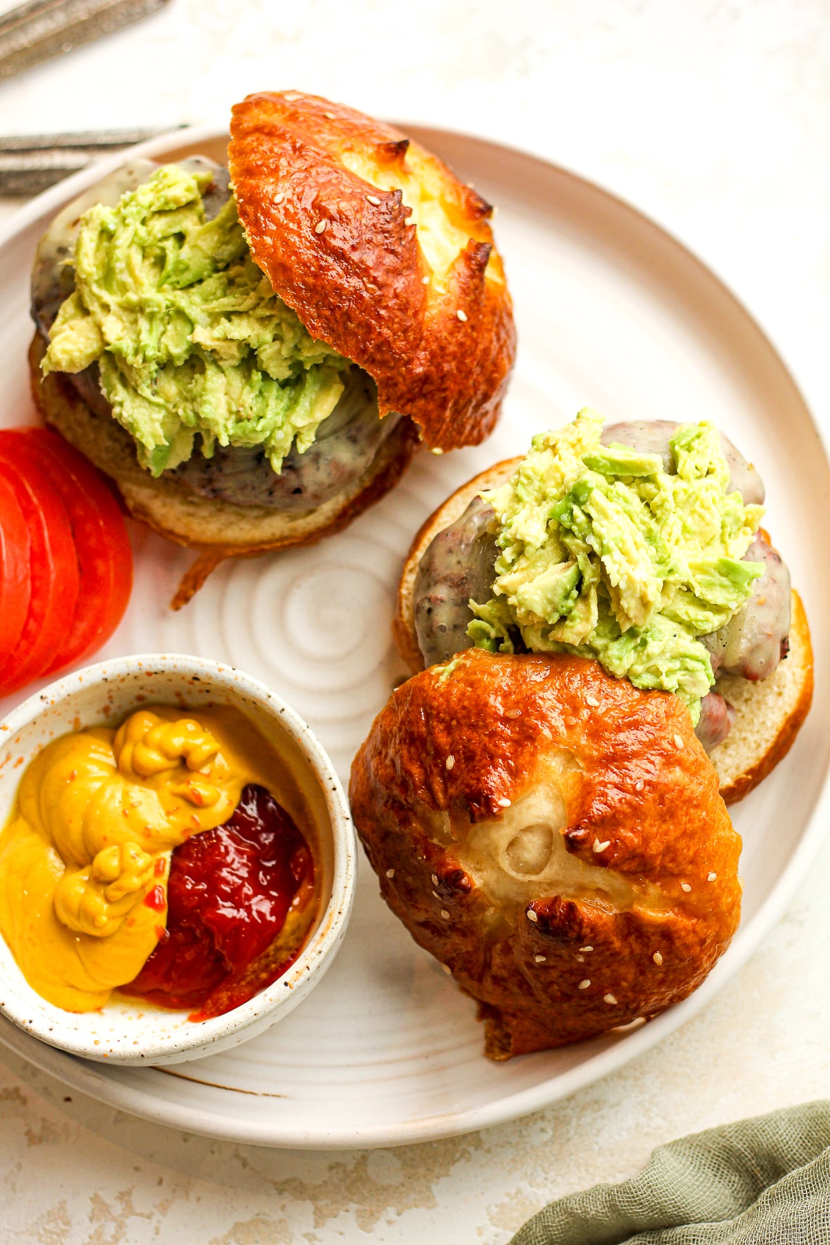 A plate with two pretzel burgers with avocado.