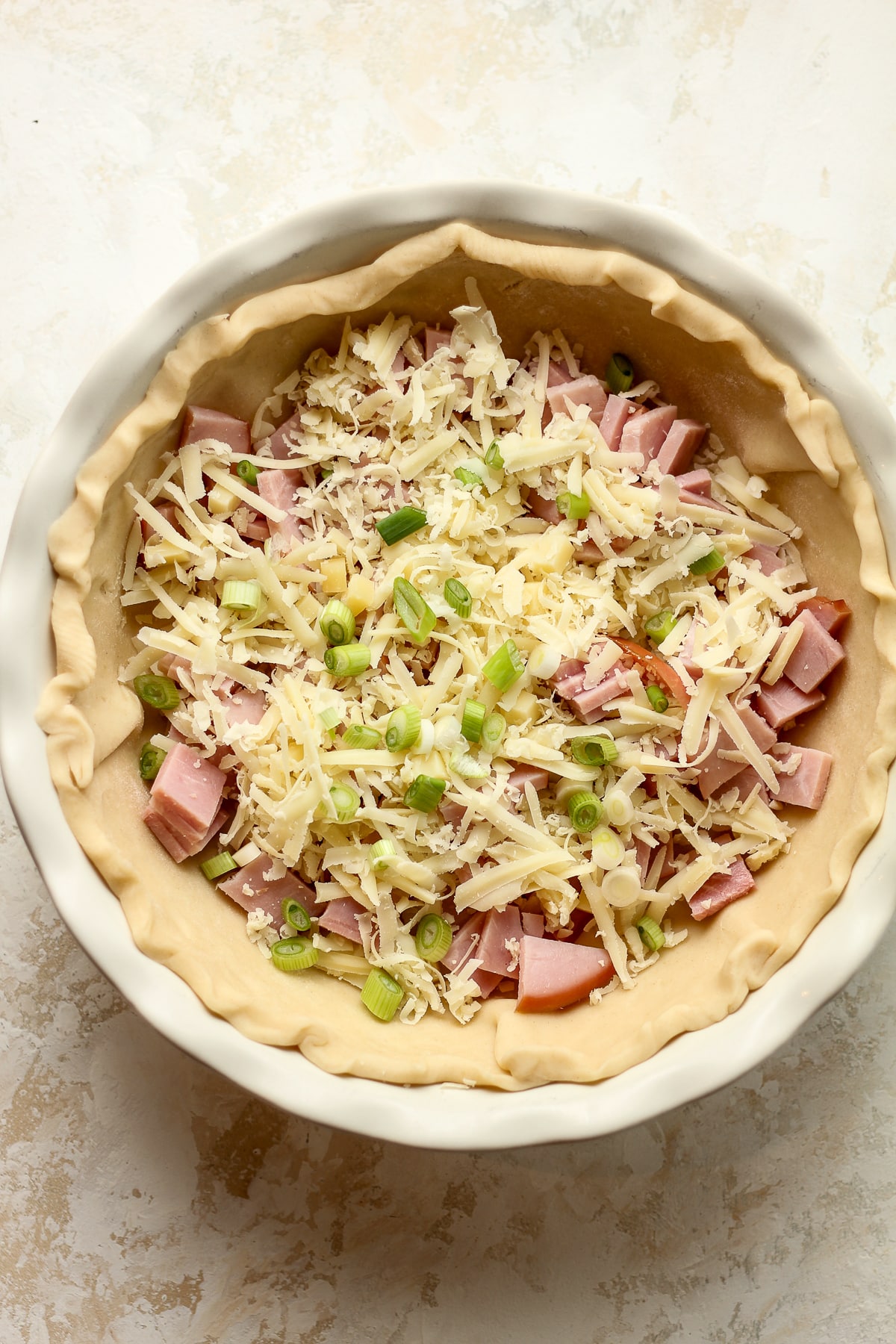 A pie crust with ham, cheese, and green onions.