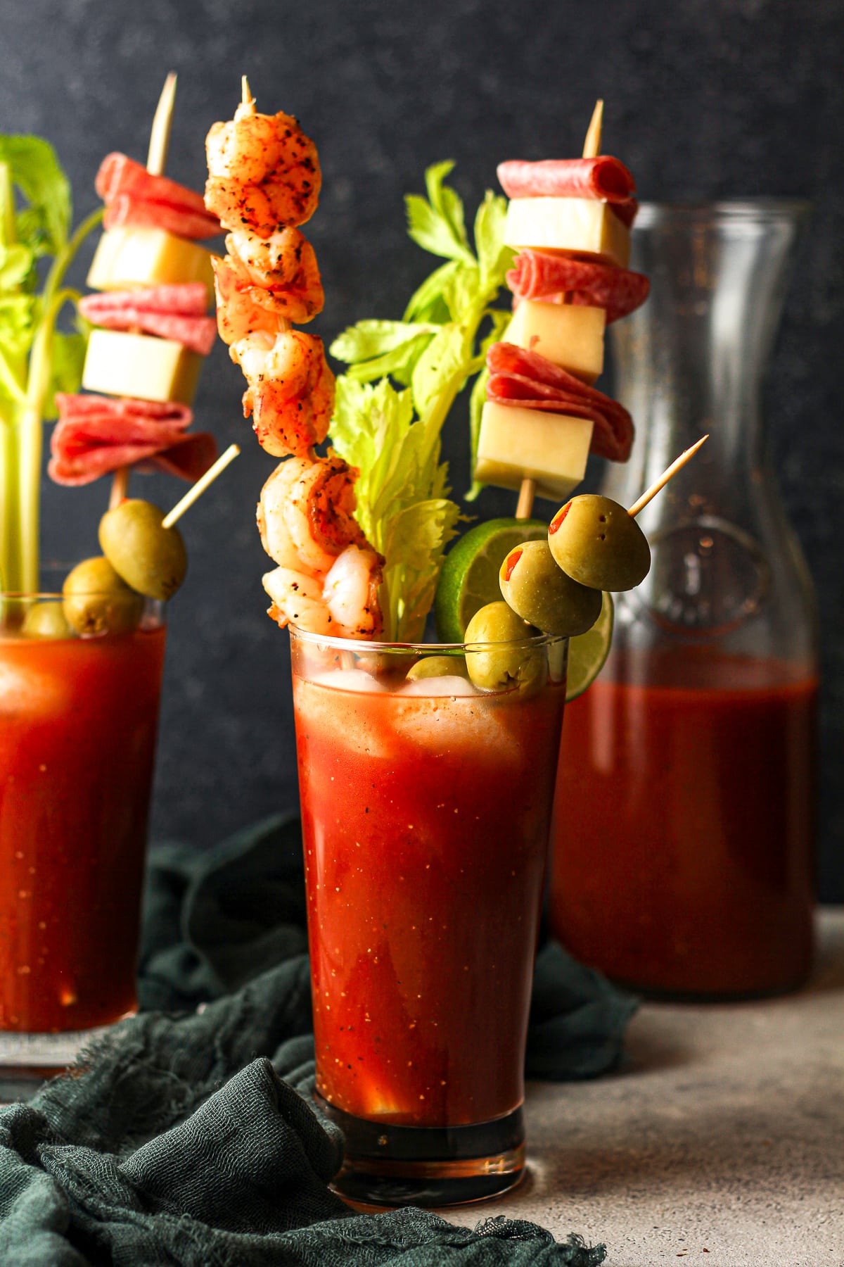Side view of two spicy bloody Marys with shrimp, celery, and olive garnishes.