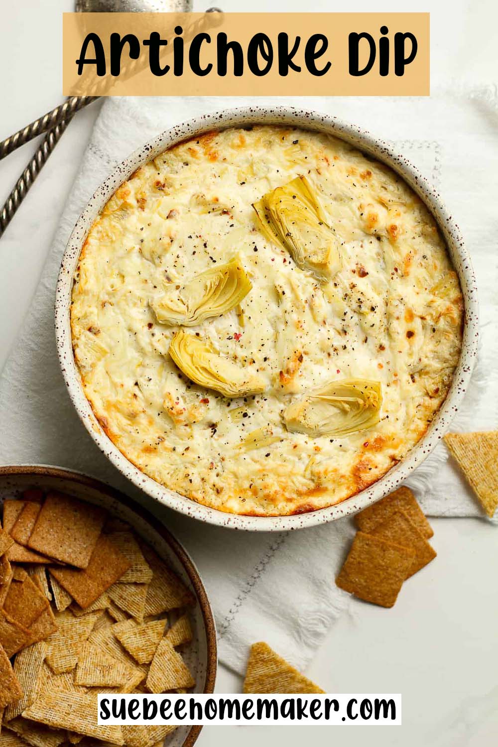 A bowl of artichoke dip with a bowl of crackers.