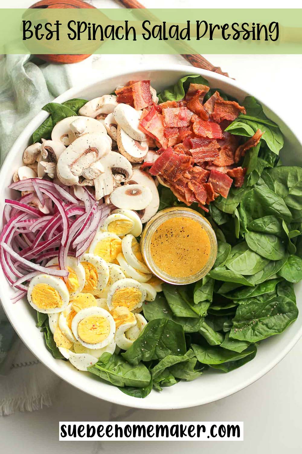 A large bowl of spinach salad with a jar of dressing.