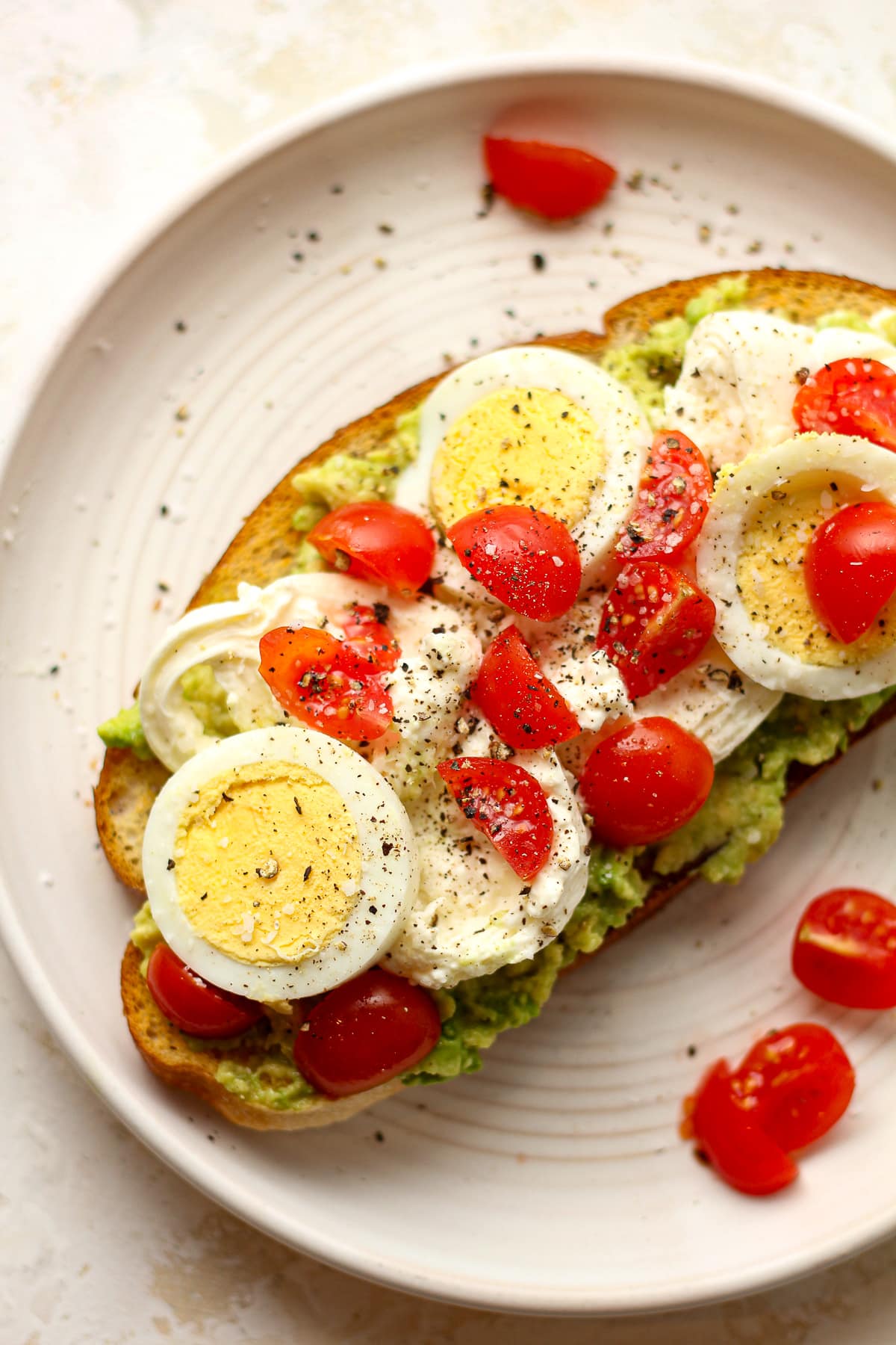 A plate of burrata toast with avocado and egg, plus tomatoes.