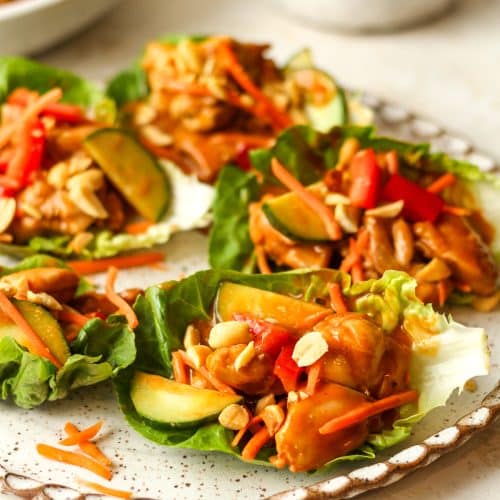 Side view of several chicken lettuce wraps with peanuts on top.